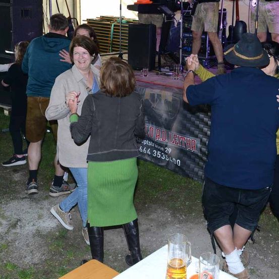 Eine Gruppe von Menschen tanzt bei einem Outdoor-Event. Eine Person hält ein Glas Bier.