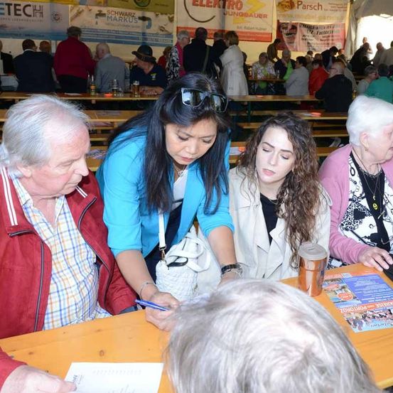 Eine Frau sitzt an einem Tisch mit einem Mann und einer Frau. Die Frau schreibt auf ein Stück Papier. Sie melden sich wahrscheinlich für eine Veranstaltung an.