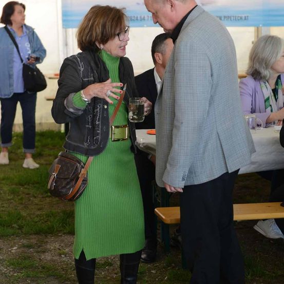 Eine Frau in einem grünen Kleid spricht mit einem Mann in einem Anzug bei einer Veranstaltung im Freien.
