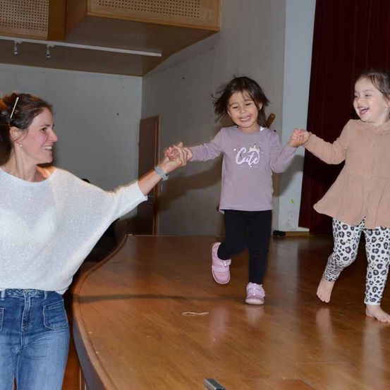 Eine Frau hält die Hände von zwei Kindern auf der Bühne, sie scheinen alle eine tolle Zeit zu haben.