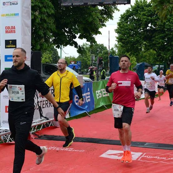 Ein Marathonlauf findet auf einer roten Bahn statt, mit Läufern, die Startnummern tragen, umgeben von Bannern und einer Menge.