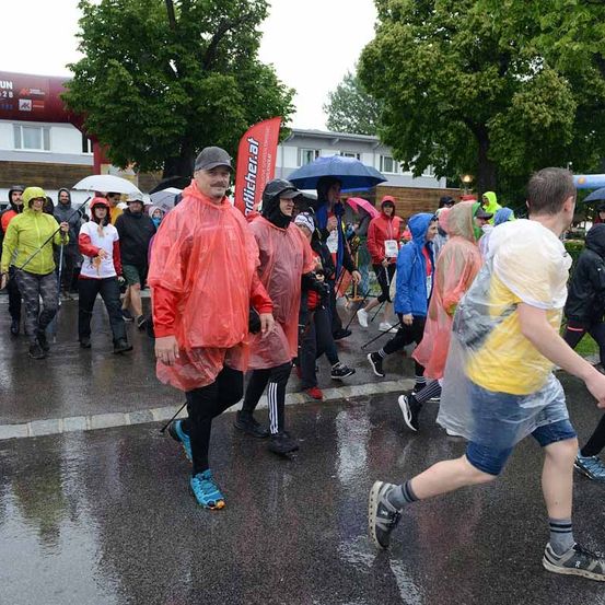 Marathonteilnehmer tragen Regenmäntel und Plastikponchos. Ein rotes Banner ist im Hintergrund zu sehen.