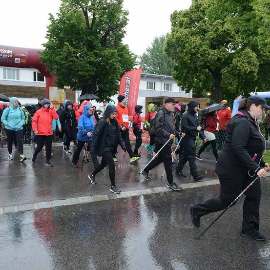 Marathonteilnehmer laufen bei Regen. Sie tragen Regenmäntel und benutzen Regenschirme. Der Weg ist nass.