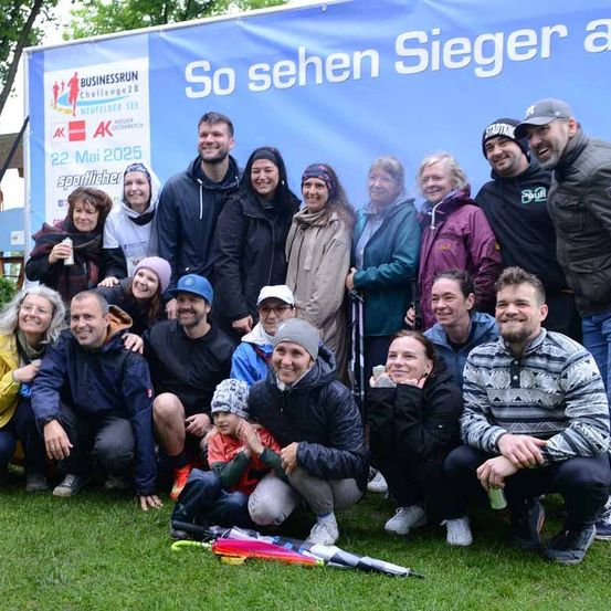 Eine Gruppe von Menschen in Winterkleidung posiert für ein Foto vor einem Banner, auf dem 'So sehen Sieger an' steht. Das Banner ist blau mit weißen Text.