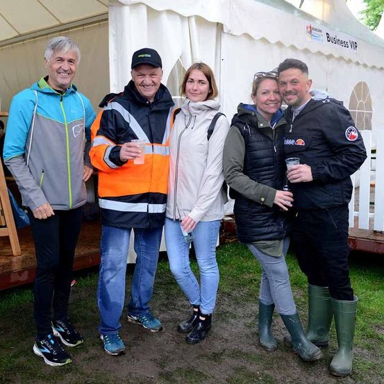 Fünf Personen stehen gemeinsam vor einem weißen Zelt mit der Aufschrift Business VIP. Sie lächeln und scheinen für ein Foto zu posieren.