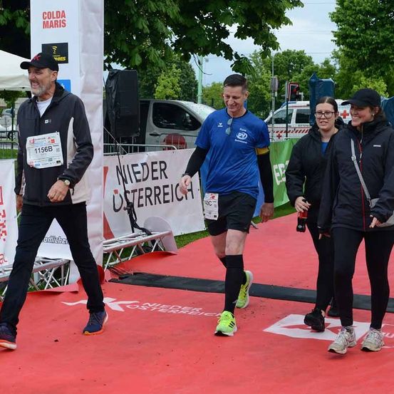 Läufer überqueren die Ziellinie eines Marathons, tragen nummerierte Startnummern und Turnschuhe. Ein Läufer lächelt.