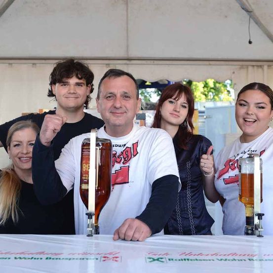 Fünf Personen posieren für ein Foto, zwei Frauen zeigen den Daumen hoch, ein Mann hält einen Bierhahn und zwei Frauen lächeln in einem Zelt.
