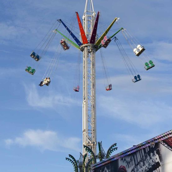 Ein bunter Hochschaukel-Ride unter blauem Himmel mit verstreuten Wolken. Die Schaukel hat mehrere Sitze, die an Ketten befestigt sind und ist hoch in der Luft gelegen.