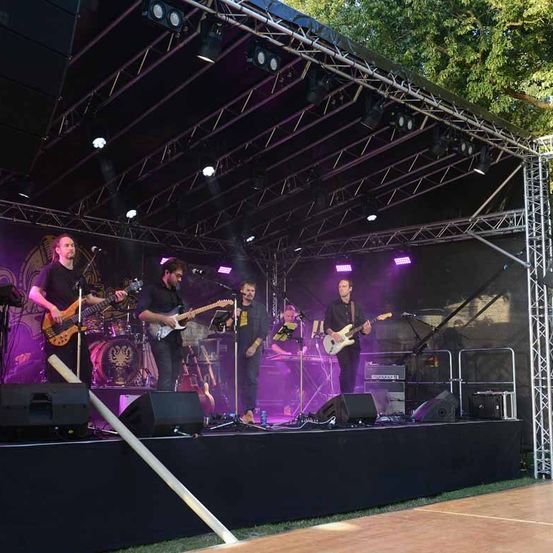 Eine Band mit vier Mitgliedern tritt auf einer Bühne mit lila Beleuchtung auf. Sie spielen Gitarren und andere Instrumente.