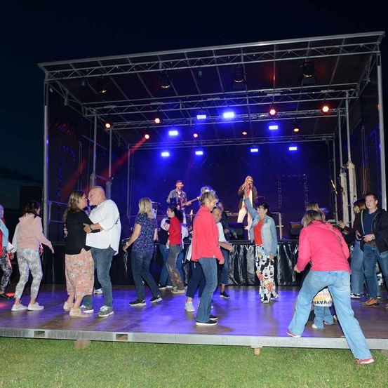 Eine Nachtveranstaltung mit Bühne, blauer Beleuchtung und tanzenden Menschen. Eine Frau singt und ein Mann spielt Gitarre.