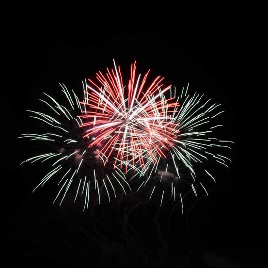 Ein Feuerwerk explodiert in der Nacht am Himmel und erzeugt helle rote, weiße und grüne Farben vor einem dunklen Hintergrund.