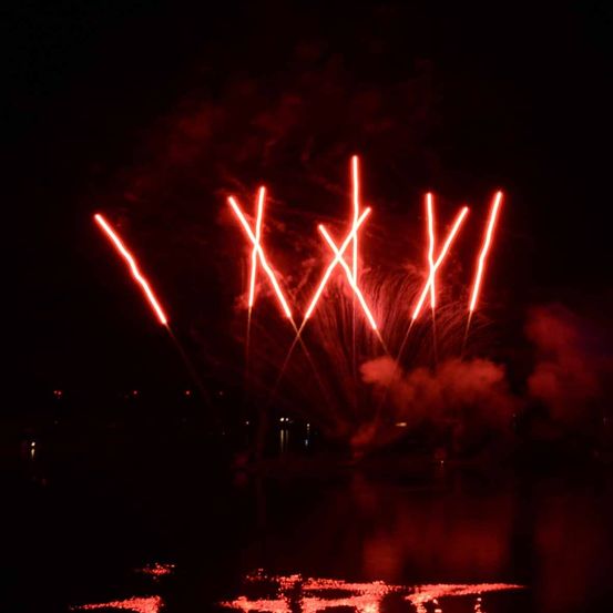 Ein nächtliches Feuerwerk mit roten Lichtern, die 'XIV' am Himmel über einem dunklen Gewässer bilden.