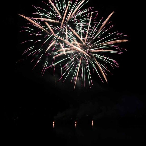 Ein leuchtendes Feuerwerk explodiert in der Nacht, der Himmel wird von verschiedenen Farben und Formen erhellt.