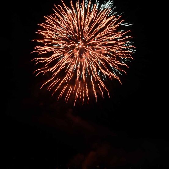Ein helles, farbenfrohes Feuerwerk erleuchtet den Nachthimmel mit roten, orangefarbenen und blauen Farbtönen.