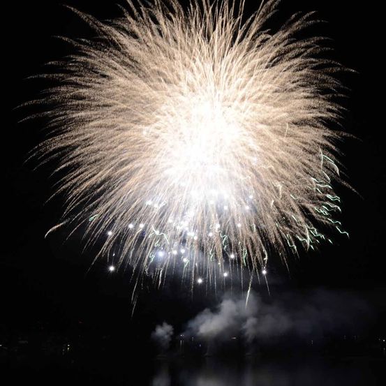 Ein Nachthimmel erfüllt von einem blendenden Feuerwerk, das den dunklen Hintergrund mit leuchtenden Farben und Rauch beleuchtet.