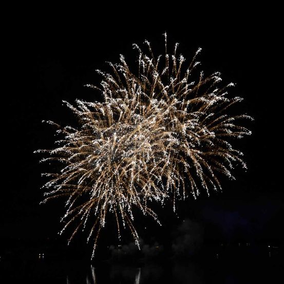 Ein Nachthimmel, der von einem goldenen Feuerwerk mit funkelnden Effekten beleuchtet wird. Das Feuerwerk zeigt ein kreisförmiges Muster mit nach außen strahlenden Funken.