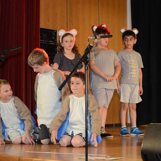 Fünf Kinder in Kostümen stehen auf der Bühne mit Mikrofon und Lautsprecher, zwei Mädchen mit Ohren, zwei Jungen vor ihnen kniend und ein Junge im Stehen.