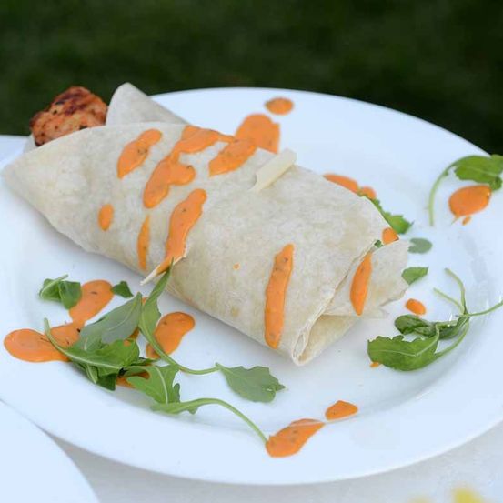 Ein Burrito mit Käse und oranger Sauce auf einem weißen Teller mit einigen grünen Blättern.