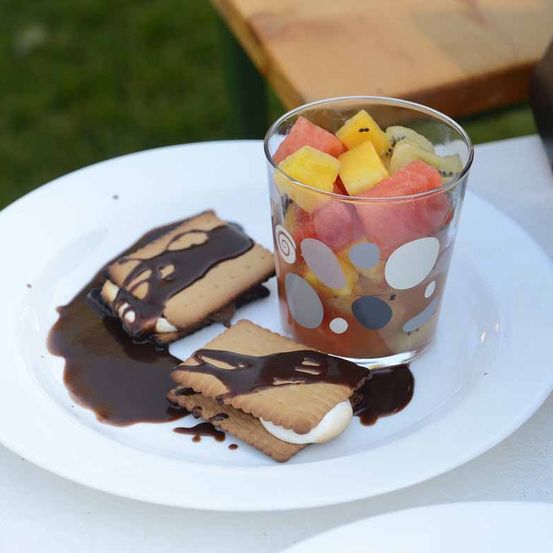 Ein weißer Teller mit einem Glas Fruchtsalat und zwei Graham-Crackern mit Schokoladenüberzug. Im Hintergrund befindet sich ein Holztisch.