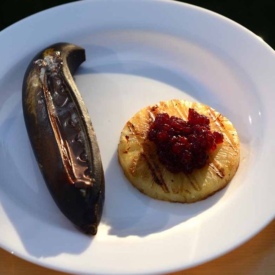 Ein weißer Teller enthält eine gegrillte Ananasscheibe mit Cranberrysauce und eine schwarze Bananenscheibe.