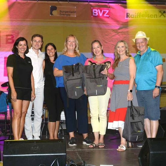 Eine Gruppe von Menschen steht mit Taschen auf der Bühne. Sie scheinen Auszeichnungen zu erhalten. Ein Banner hinter ihnen hat Logos für Burgenland Energie, BVZ und Raiffeisen.