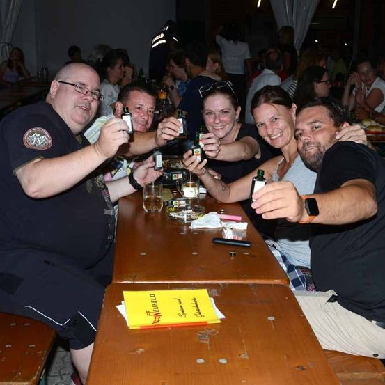 Eine Gruppe von Menschen sitzt an einem Tisch und hält Flaschen. Sie lächeln und scheinen für ein Foto zu posieren.