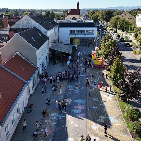 Eine Luftaufnahme einer Stadt mit Menschen, die auf der Straße und dem Bürgersteig gehen. Es gibt Gebäude, Autos und Bäume in der Gegend.