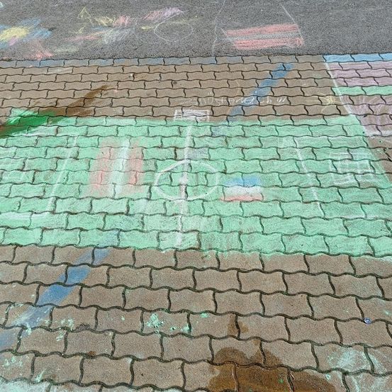 Ein gepflasterter Weg mit grünen und blauen Kreidezeichnungen, einschließlich eines Fußballfeldes und einiger Texte. Der Boden ist nass, möglicherweise vom Regen.