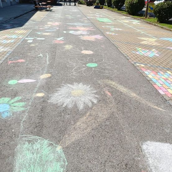 Ein Bürgersteig mit bunten Kreidezeichnungen von Blumen und anderen Designs. In der Nähe sind Bänke und Tische. Der Bürgersteig ist leer.