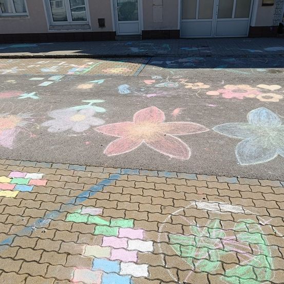 Kreidezeichnungen von Blumen und Quadraten sind auf dem Bürgersteig vor einem Gebäude mit zwei Türen. Der Bürgersteig besteht aus Ziegelsteinen.