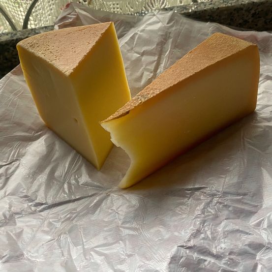 Zwei Stückchen gelben Käses liegen auf einem weißen Plastiktuch, mit einer leichten Bräunung an den Kanten. Der Käse hat eine glatte Textur und ist in zwei ungleiche Stücke geschnitten.