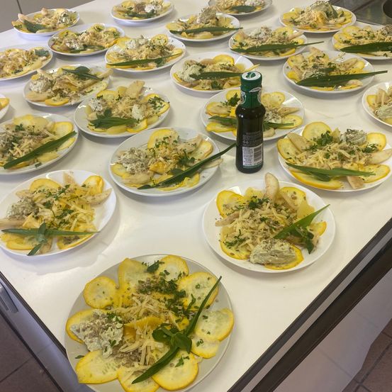 Ein Tisch zeigt mehrere Teller mit Essen, jeder mit gelben und grünen Gemüsesorten, Käse und Kräutern, mit einer Ölflasche in der Mitte.