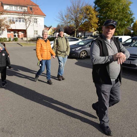 Eine Gruppe von Menschen geht auf einem Parkplatz, mit einem Gebäude und geparkten Autos im Hintergrund.
