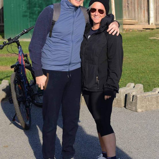 Ein Mann und eine Frau stehen auf einem Pfad mit einem Fahrrad hinter ihnen. Sie lächeln beide und posieren für ein Foto.