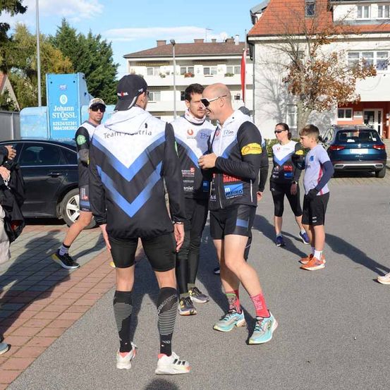 Eine Gruppe von Radfahrern in Sportbekleidung geht auf einem Außengelände. Sie sind in der Nähe eines Gebäudes mit einem Baum und einem geparkten Auto.