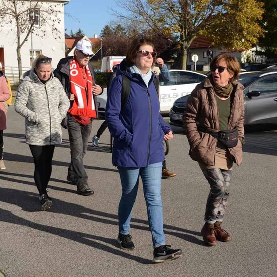 Eine Gruppe von Menschen geht gemeinsam auf einem Parkplatz, mit Autos und Gebäuden im Hintergrund.
