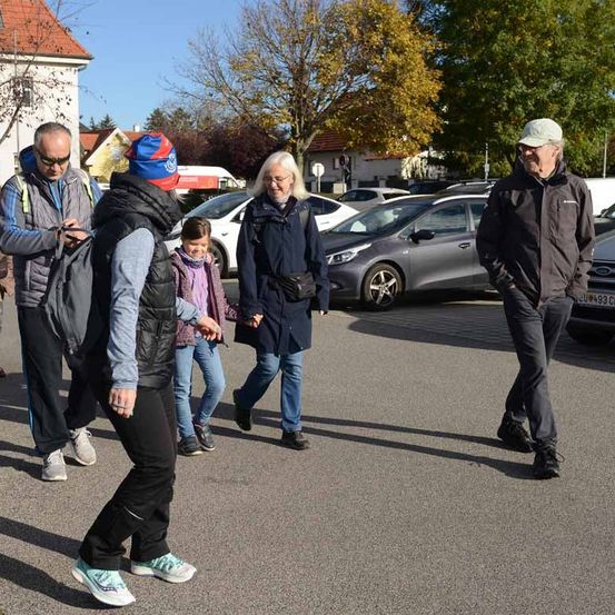 Eine Gruppe von Menschen geht auf einem Parkplatz. Eine Frau hält ein Kind an der Hand.