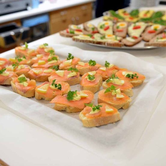 Ein Tisch mit mehreren Tabletts von Canapes mit Räucherlachs, Zitrone und Kräutern in einer Küchenumgebung.