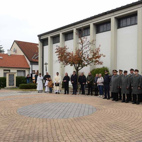 Eine Gruppe von Menschen steht im Kreis vor einer Kirche mit zwei Priestern in weißen Roben.