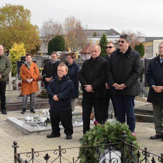 Eine Gruppe von Menschen steht tagsüber auf einem Friedhof. Sie scheinen einer Gedenkfeier beizuwohnen.