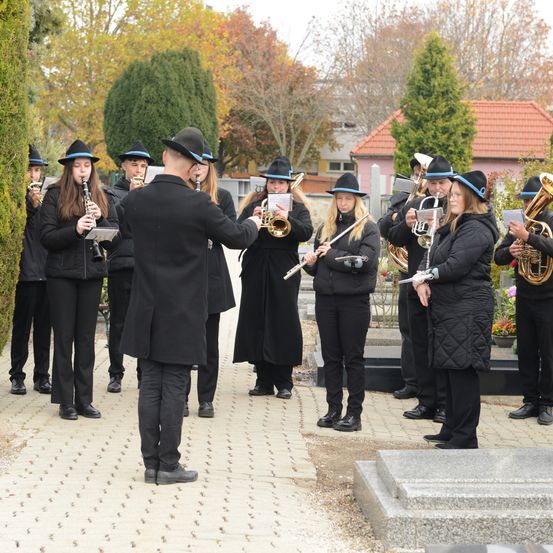 Eine Beerdigungsfeier auf einem Friedhof mit Musikern, die verschiedene Instrumente spielen, alle in Schwarz gekleidet.