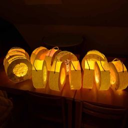 Eine Reihe kreisförmiger Papierlaternen mit aufwendigen Mustern und gelben Lichtern steht auf einem Holztisch in einem schwach beleuchteten Raum.