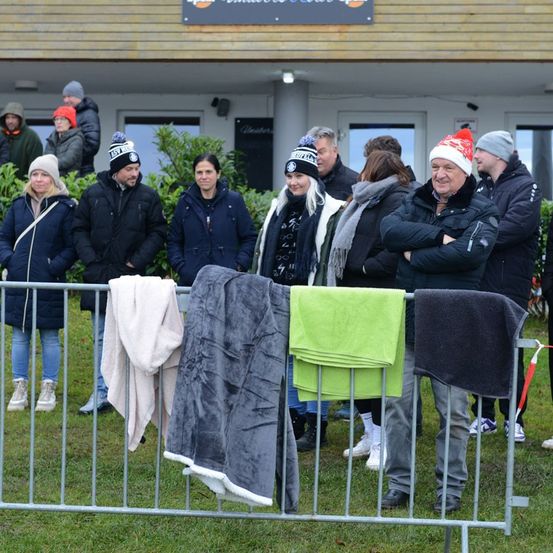 Eine Gruppe von Menschen steht hinter einem Zaun mit hängenden Winterkleidung. Sie sind alle in Winterkleidung gekleidet und scheinen auf etwas zu warten.