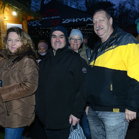 Drei Menschen stehen vor einem Zelt, eine Frau hält eine Kamera. Der Mann in der Mitte lächelt.