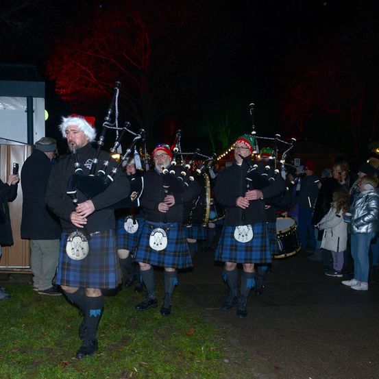 Eine Gruppe von Dudelsackspielern in Kilts tritt bei Nacht im Freien auf, während eine Zuschauermenge zusieht.