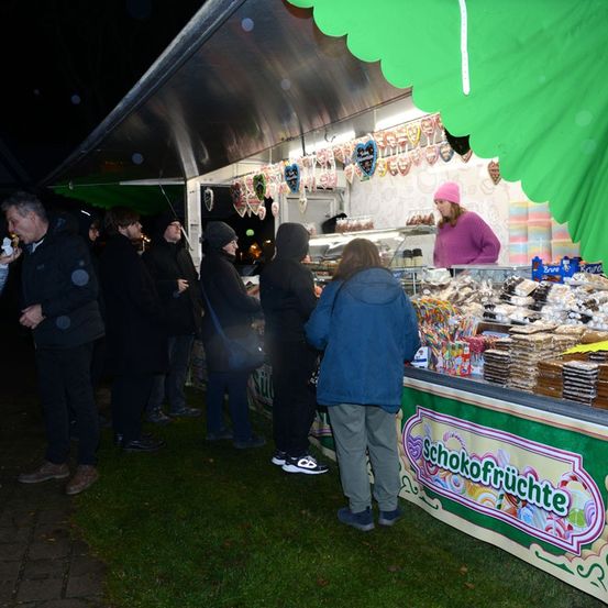 Eine Frau mit einer rosa Mütze bedient Kunden an einem Essensstand in der Nacht. Der Stand hat eine Vielzahl von Desserts und Süßigkeiten.
