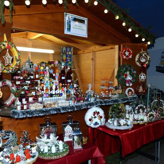 Ein Holzladen mit Weihnachtsdekorationen, die auf den Regalen und Tischen ausgestellt sind. Der Laden hat zwei Tische mit roten Tischdecken und eine weiße Laterne. Der Laden hat ein Schild, das Kunstwerk Handwerk besagt.