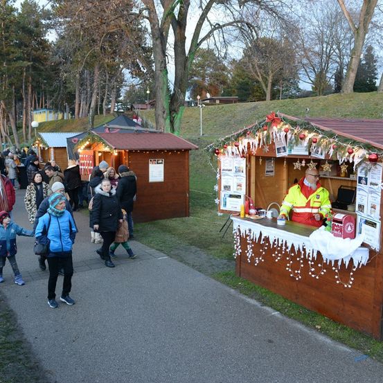 Mehrere Menschen gehen einen Gehweg entlang, mit Essensständen auf beiden Seiten, darunter einer mit Weihnachtsthema.