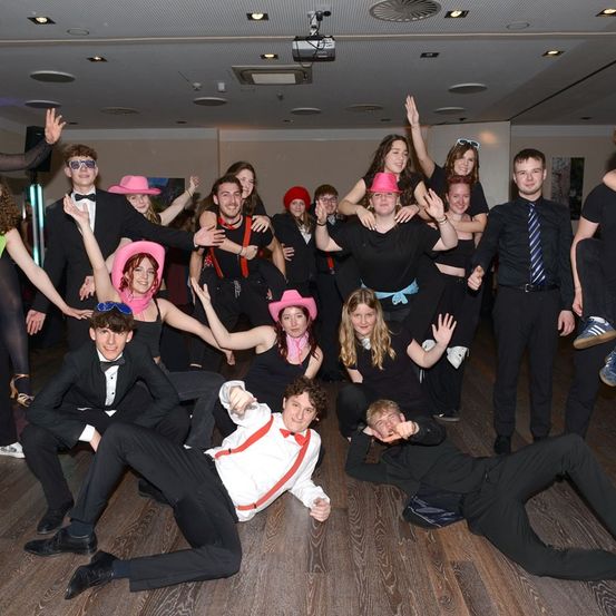 Eine Gruppe von Menschen in schwarz und mit rosa Hüten posiert für ein Foto in einem Raum mit Holzböden und Deckenleuchten.