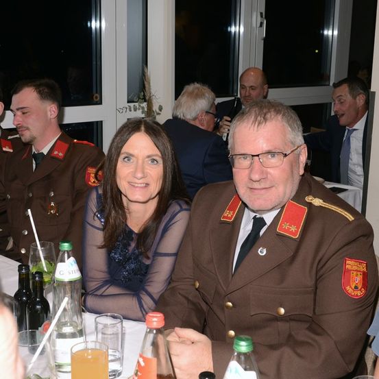 Eine Gruppe von Menschen in Militäruniformen sitzt an einem Tisch, lächelt und posiert für ein Foto. Flaschen und Gläser stehen auf dem Tisch.